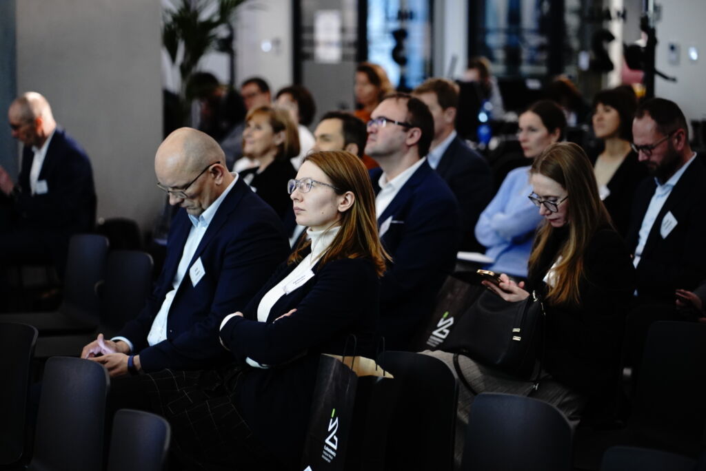 Grupa kobiet i mężczyzn na sali konferencyjnej słuchających wystąpienia