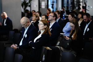 Grupa kobiet i mężczyzn na sali konferencyjnej słuchających wystąpienia