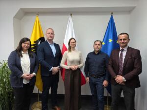 Dwie kobiety i trzech mężczyzn biorących udział w spotkaniu. Zdjęcie na tle fal UE, Polski i Województwa Dolnośląskiego